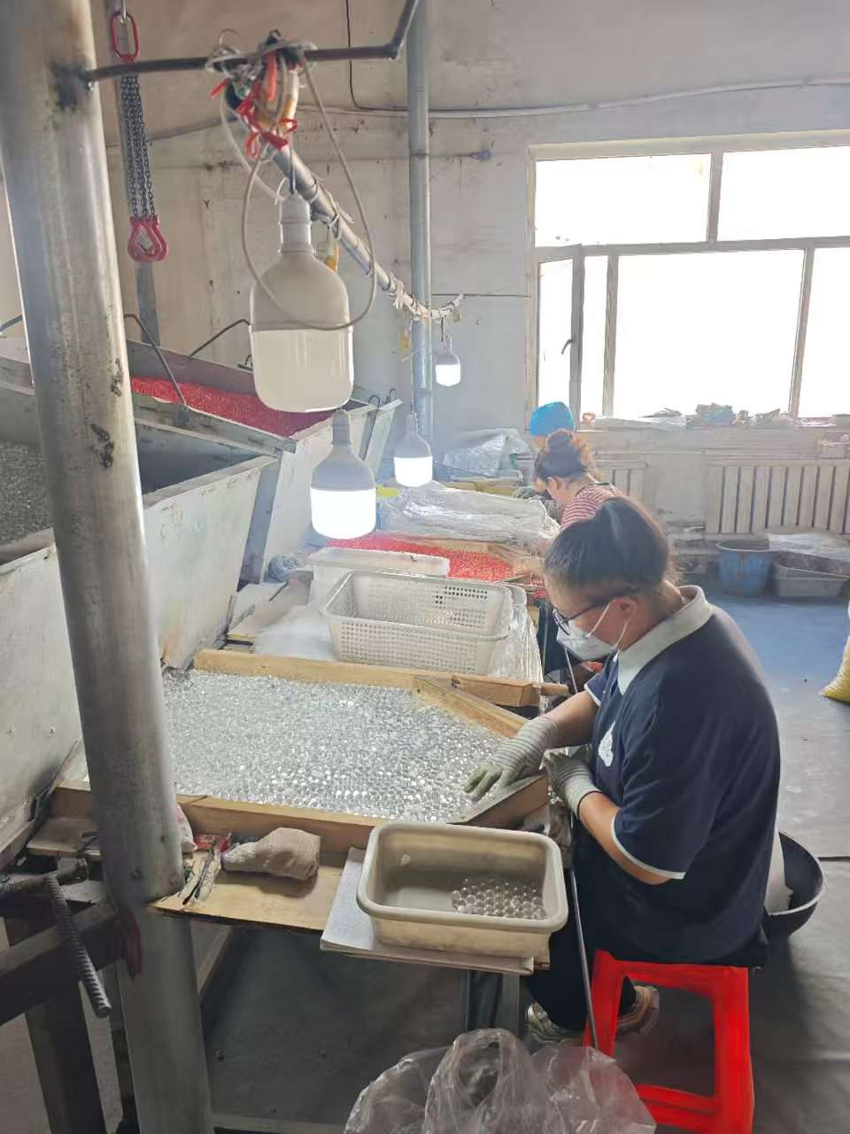 Operator hand-sorting glass beads under inspection lamps at the Jingli plant